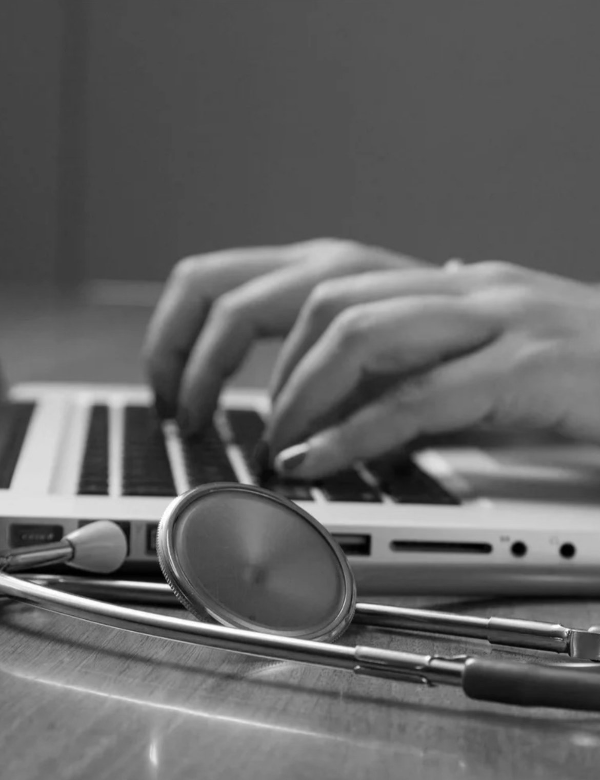 Typing at a laptop beside a stethoscope